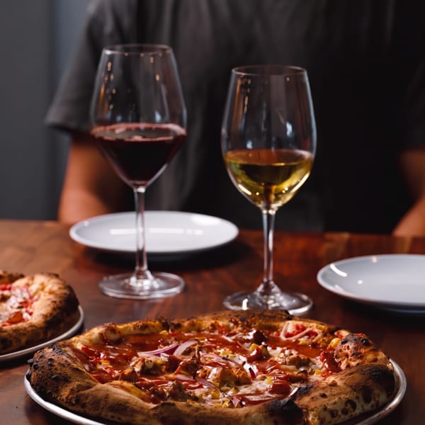 Neapolitan-style pizza with charred crust, two wine glasses, and white plates on a warmly lit restaurant table.
