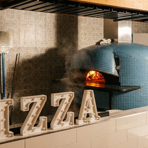 A blue tiled pizza oven with a fire burning inside, next to a stack of firewood.