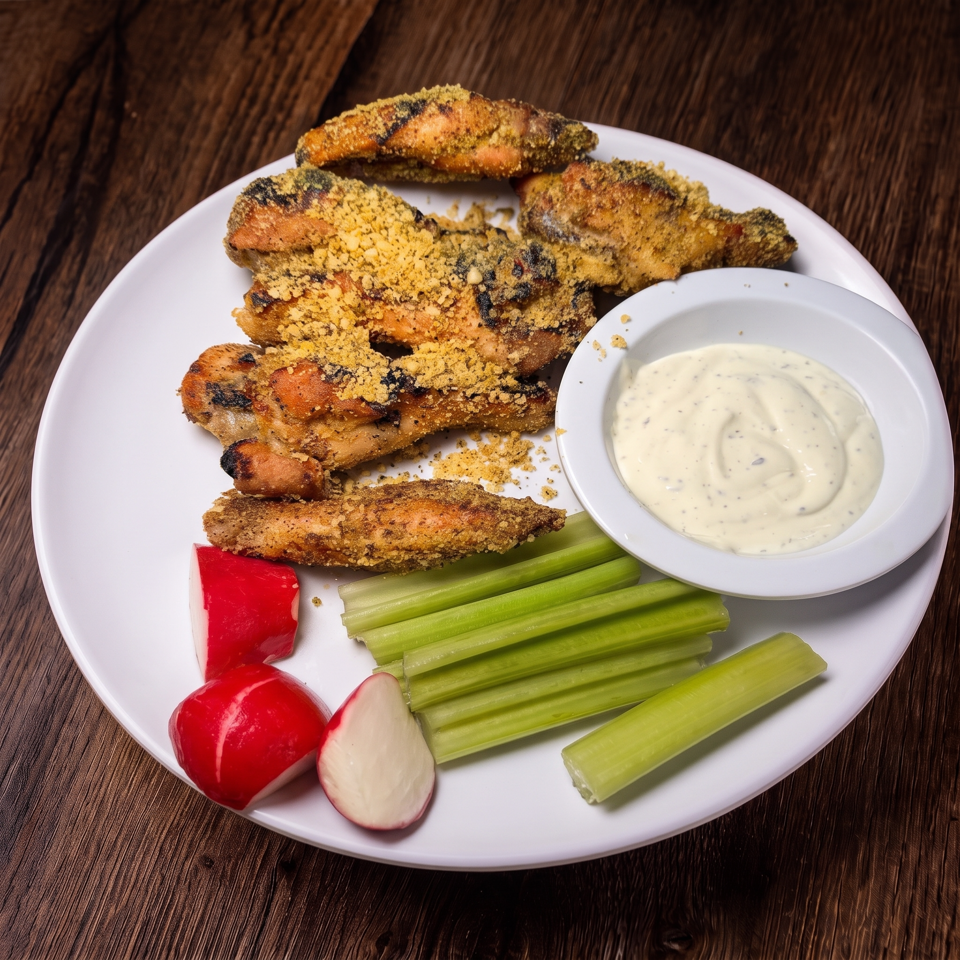 Crispy grilled chicken tenders with creamy dipping sauce, celery sticks, and radishes on a white plate.